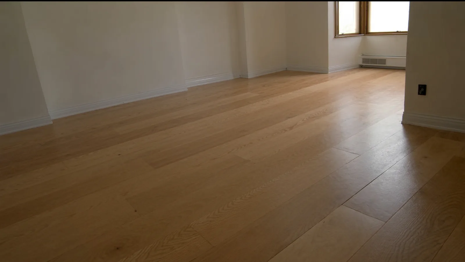 The same room after flooring installation — warm white oak engineered hardwood throughout, clean transitions to kitchen tile